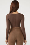 Back view of model posing in the fitted brown rib Classic Scoop Long Sleeve top with a scoop neckline and vertical stitch detail down the center back bodice